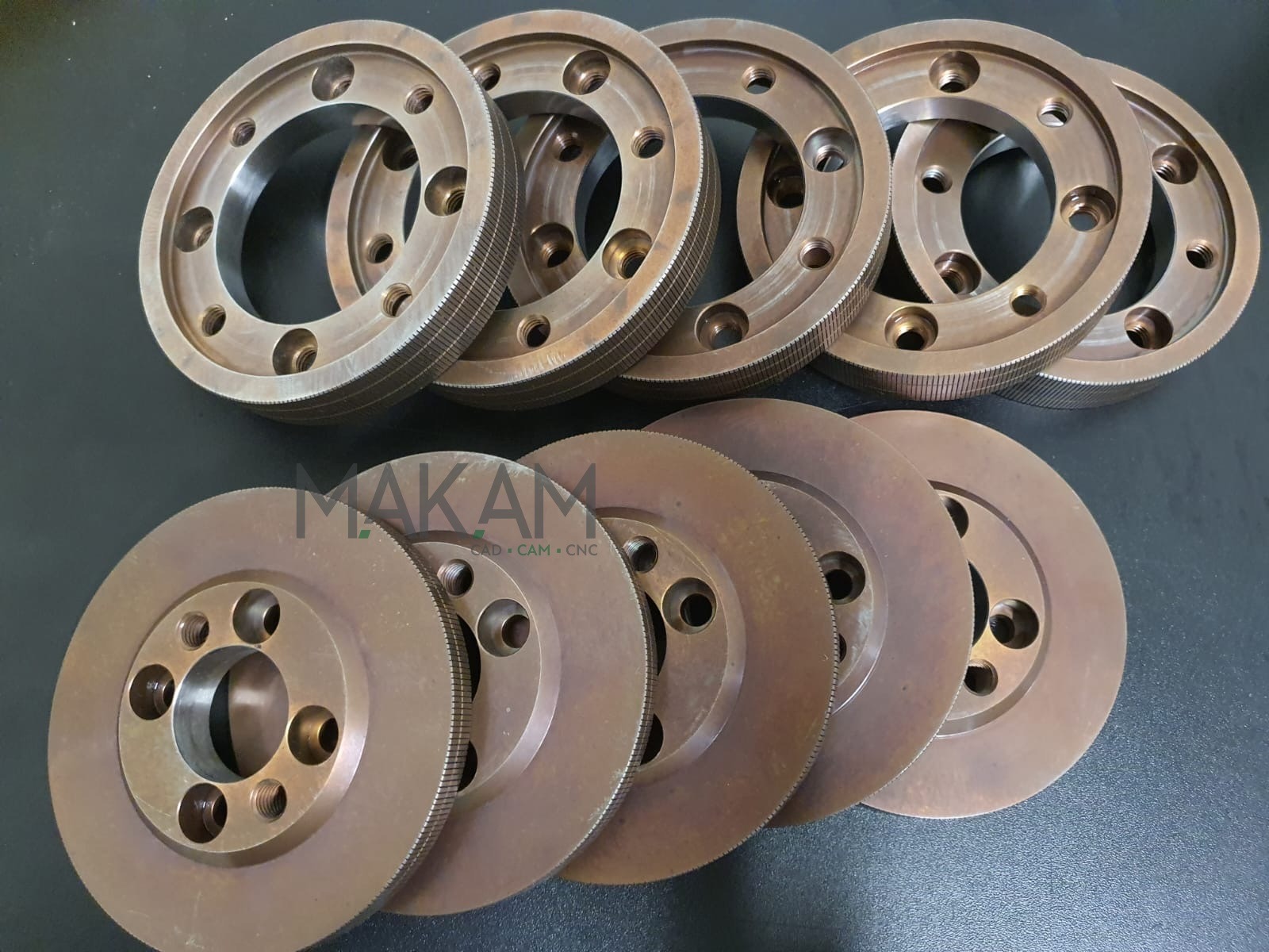 Metalowe tarcze z otworami, ułożone w dwóch rzędach, z widocznymi śladami obróbki skrawaniem na krawędziach, na ciemnym tle. Detal precyzyjnej mechaniki.