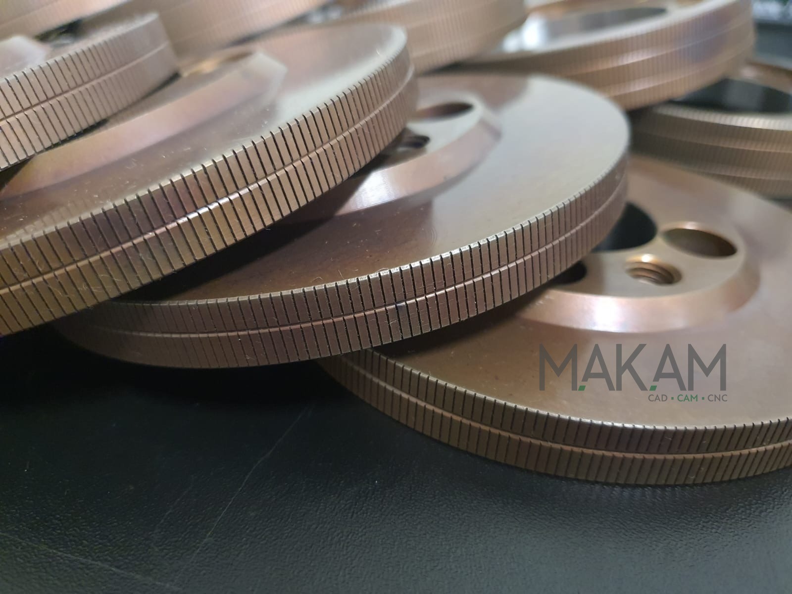 Precyzyjnie obrobione, metalowe tarcze z rowkami, ułożone warstwami, z logo MAKAM CAD CAM CNC w prawym dolnym rogu. Detal obróbki skrawaniem.