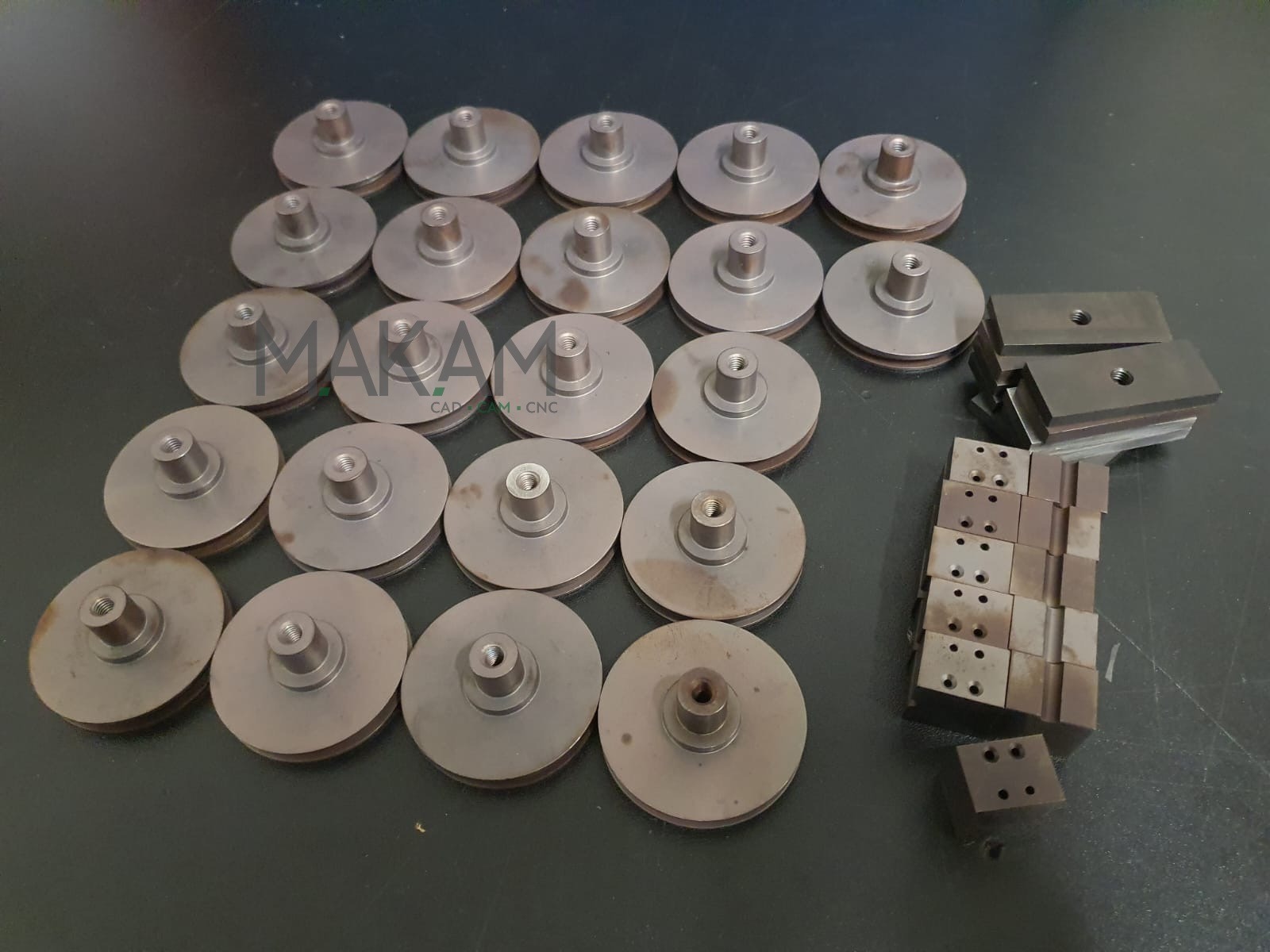 Metalowe elementy tokarskie i frezarskie ułożone na ciemnym blacie, widoczne ślady obróbki, różne kształty i rozmiary, gotowe do montażu lub dalszej obróbki.