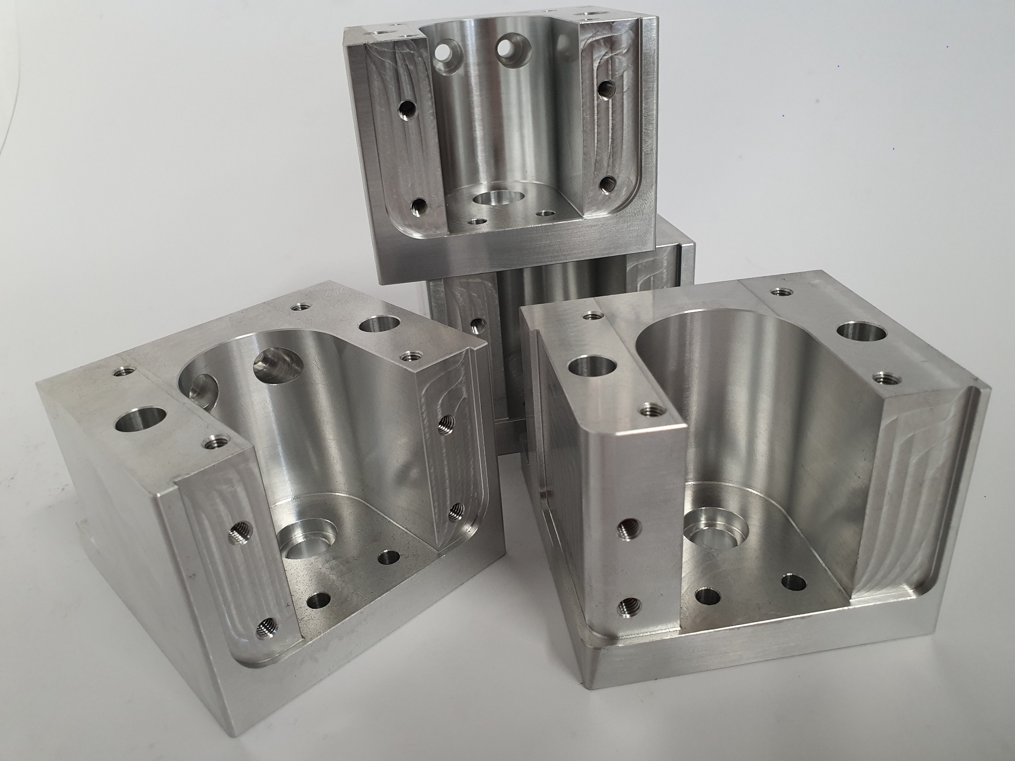 Precyzyjnie obrobione, aluminiowe elementy konstrukcyjne z licznymi otworami, ułożone na białym tle. Widoczne ślady obróbki skrawaniem.