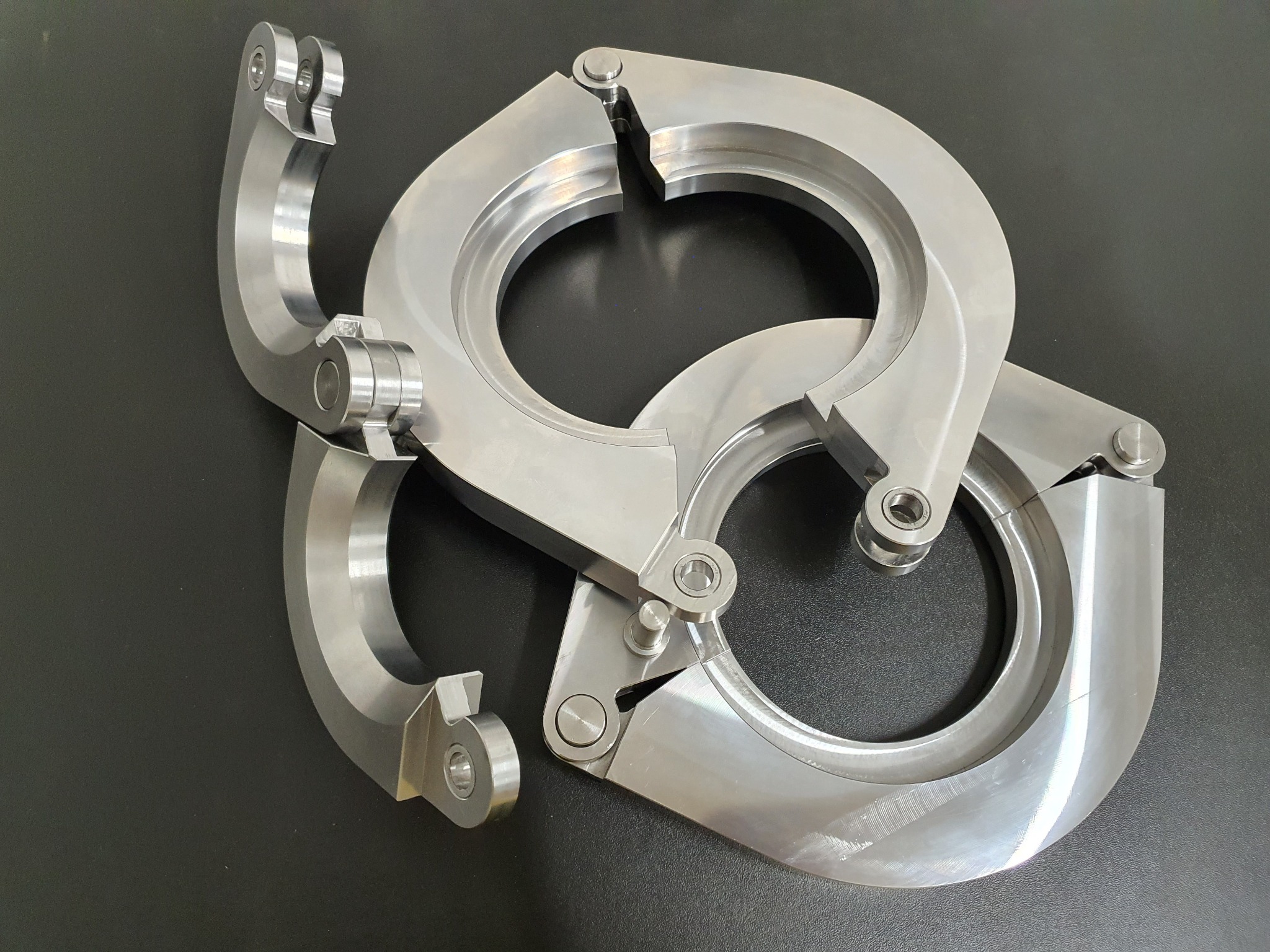 Dwa srebrne, rozłożone zaciski do elektronarzędzi na czarnym tle. Widoczne detale konstrukcyjne i precyzyjne wykonanie elementów.