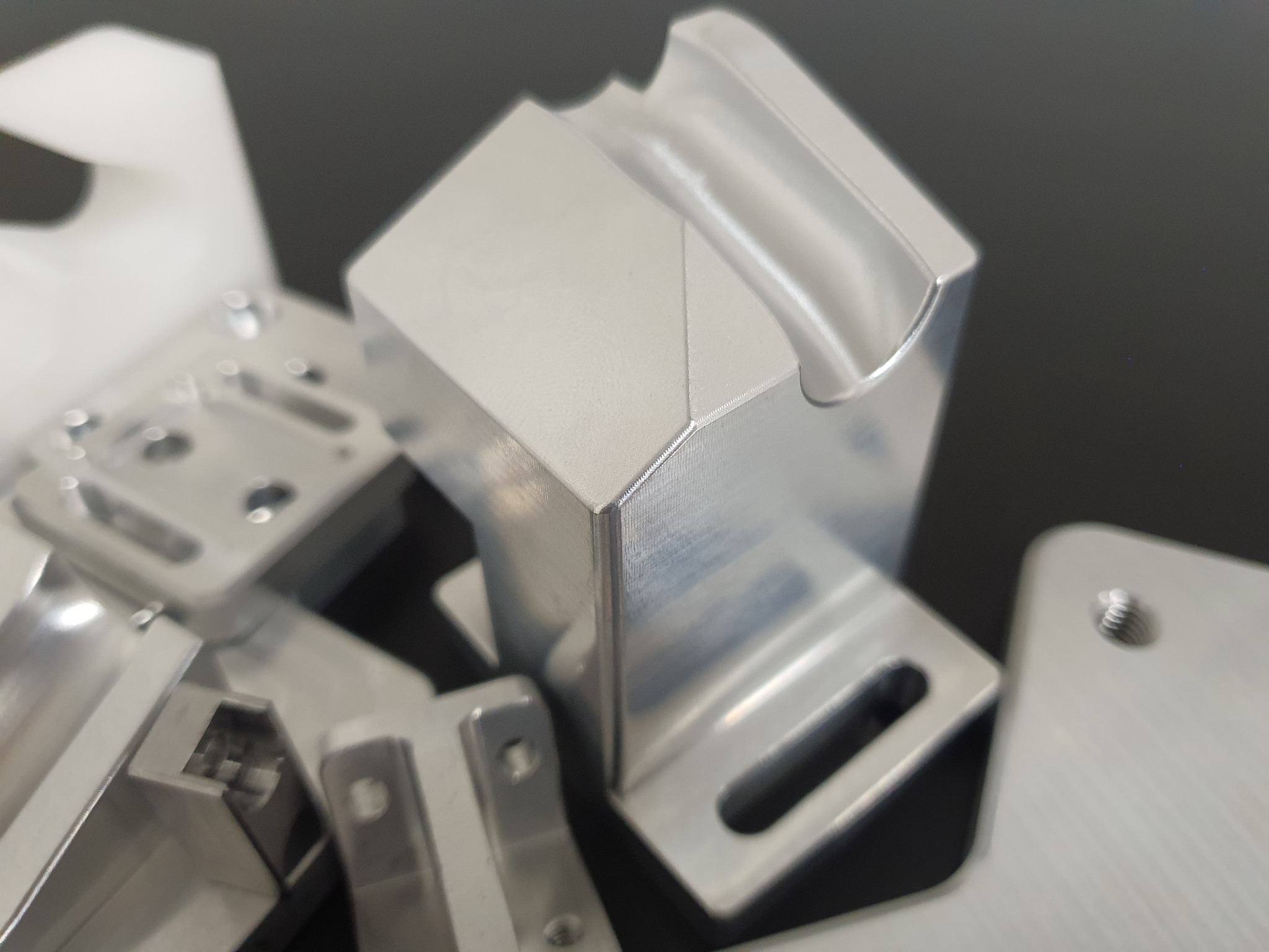 Precyzyjnie obrobione, srebrne elementy metalowe, prawdopodobnie części zamienne lub komponenty do elektronarzędzi, ułożone na ciemnym tle. Widoczne ślady obróbki.