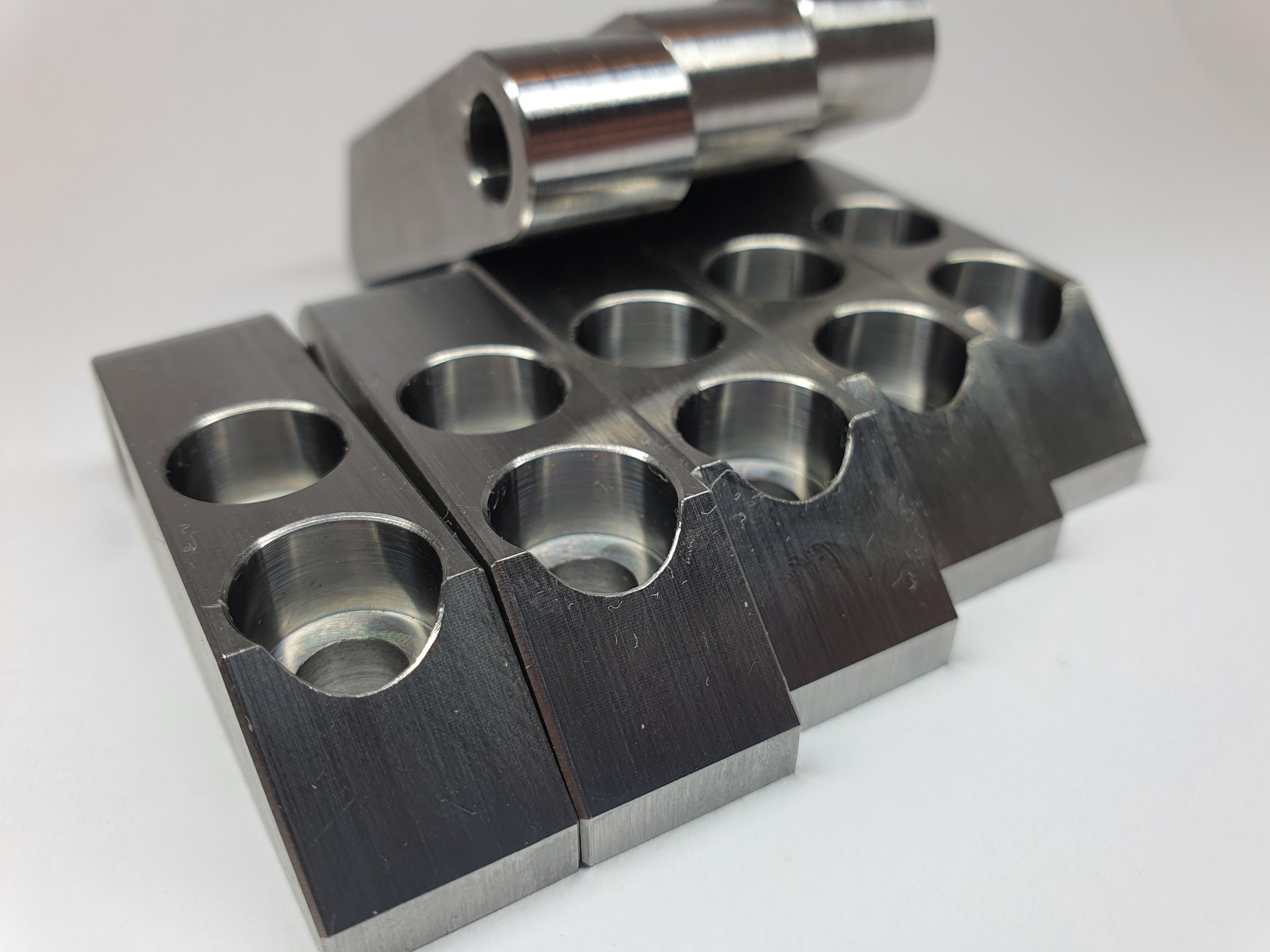 Szereg metalowych, obrobionych elementów z otworami i wycięciami, ułożonych na białym tle, ukazujących precyzyjną obróbkę skrawaniem.