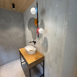 KUB - HOUSE Jakub Piechowicz - Minimalistyczna łazienka w Żywcu z umywalką na drewnianym blacie, lustrem o nieregularnym kształcie i białymi płytkami na ścianie, oświetlona wiszącą lampą.