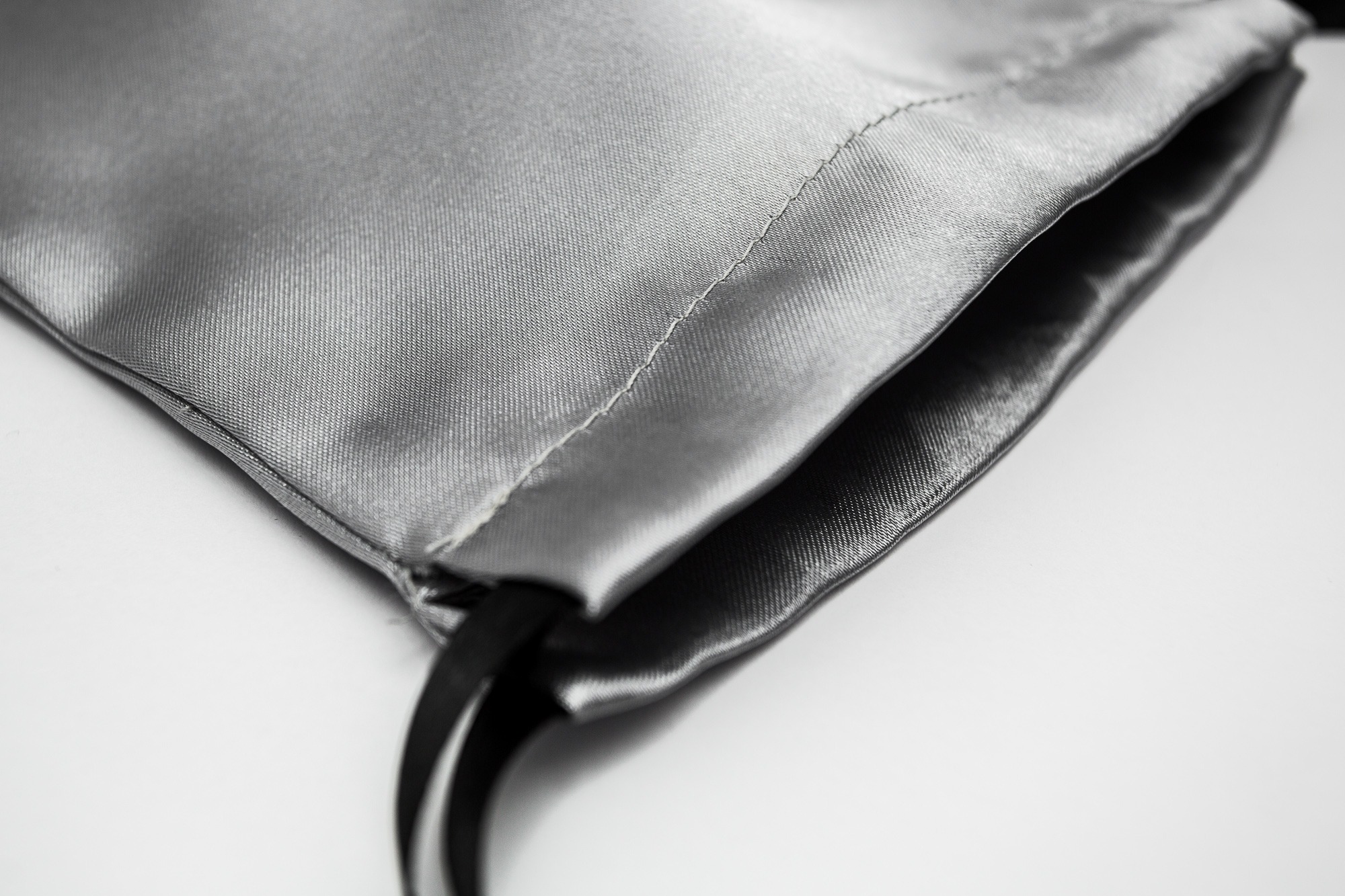 Szary satynowy woreczek ze ściągaczem, widoczne szwy i czarne sznurki, zbliżenie na fakturę materiału.