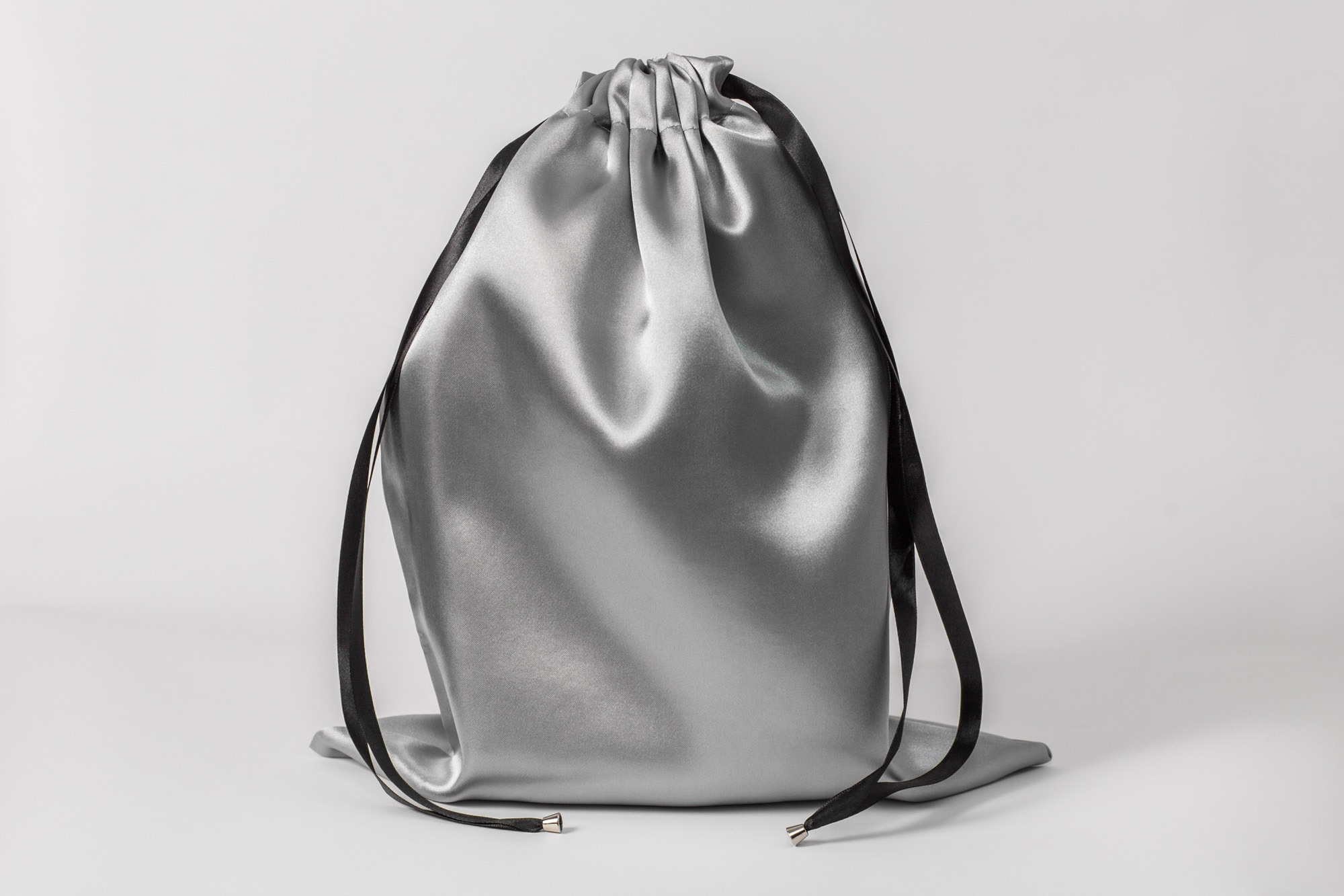 Błyszczący, srebrny worek ze ściągaczem z czarnych sznurków, leżący na białym tle.