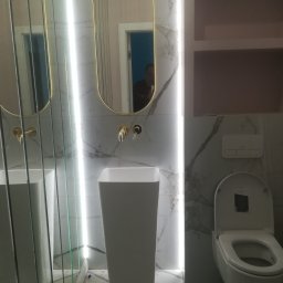 DAST - Nowoczesna łazienka z marmurowymi płytkami, owalnymi lustrami w złotych ramach, wolnostojącą umywalką i podświetleniem LED, ukazująca minimalistyczny design i eleganckie wykończenie.