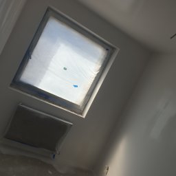 DAST - Poddasze z dwoma oknami dachowymi zabezpieczonymi folią i taśmą malarską przed malowaniem ścian na biało, widoczne ślady gładzi na podłodze.