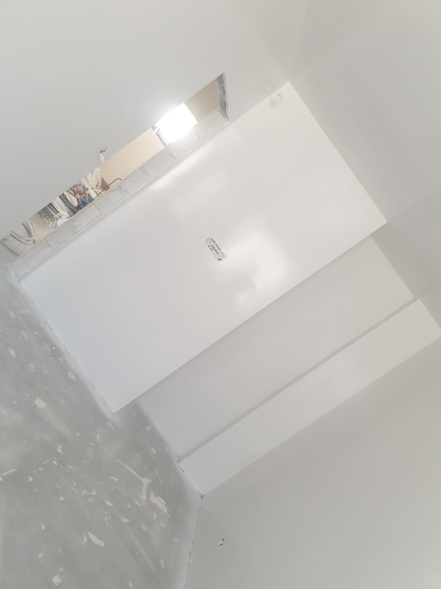Świeżo pomalowany na biało sufit z widocznym otworem instalacyjnym i fragmentem ściany z plamami po gładzi.