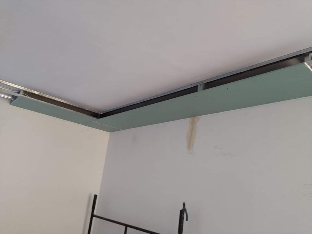 Instalacja sufitu podwieszanego z płyt gipsowo-kartonowych na metalowej konstrukcji w rogu pomieszczenia, widoczne niedoskonałości na ścianie.