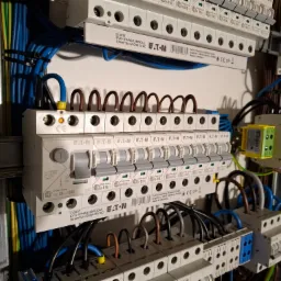 Rozdzielnica elektryczna marki Eaton z widocznymi bezpiecznikami, przewodami w kolorach niebieskim, brązowym i żółto-zielonym, starannie ułożonymi i podłączonymi do listew zaciskowych.