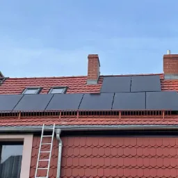 Czerwony dach domu z zamontowanymi panelami słonecznymi; drabina oparta o rynnę.