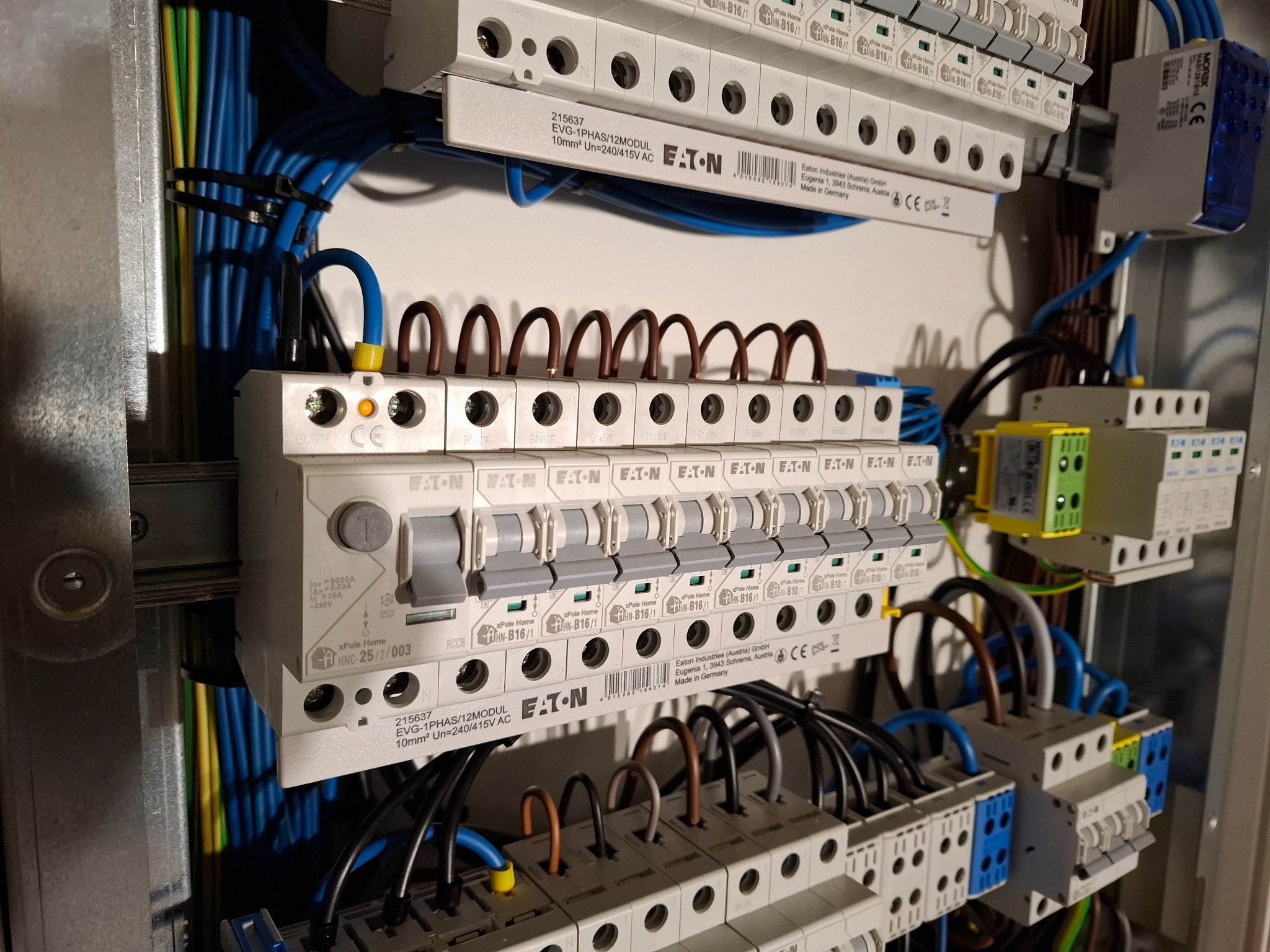 Rozdzielnica elektryczna marki Eaton z widocznymi bezpiecznikami, przewodami w kolorach niebieskim, brązowym i żółto-zielonym, starannie ułożonymi i podłączonymi do listew zaciskowych.