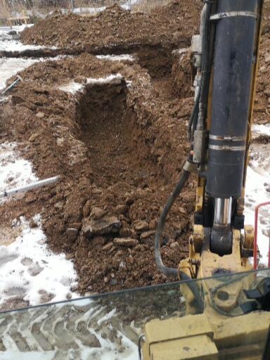 Wykonany wykop pod fundamenty z widocznym ramieniem koparki i resztkami śniegu na ziemi.