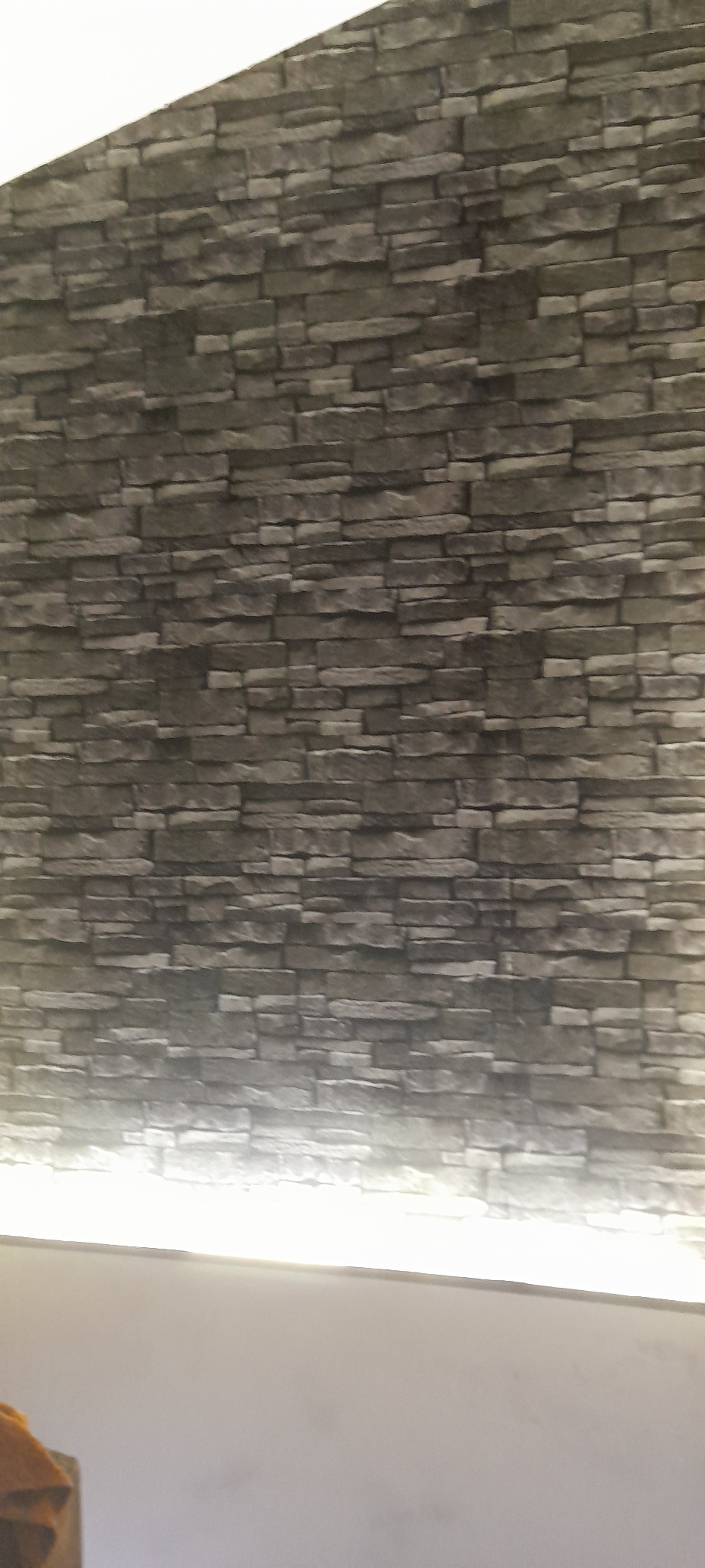 Szara ściana imitująca kamień z podświetleniem LED u dołu, tworząca nowoczesny efekt dekoracyjny.