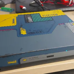 Modyfikowana konsola Xbox z motywem cyberpunkowym, z żółto-niebieską obudową ozdobioną napisami i wzorami technicznymi, leżąca na biurku obok kontrolera i innych akcesoriów komputerowych.