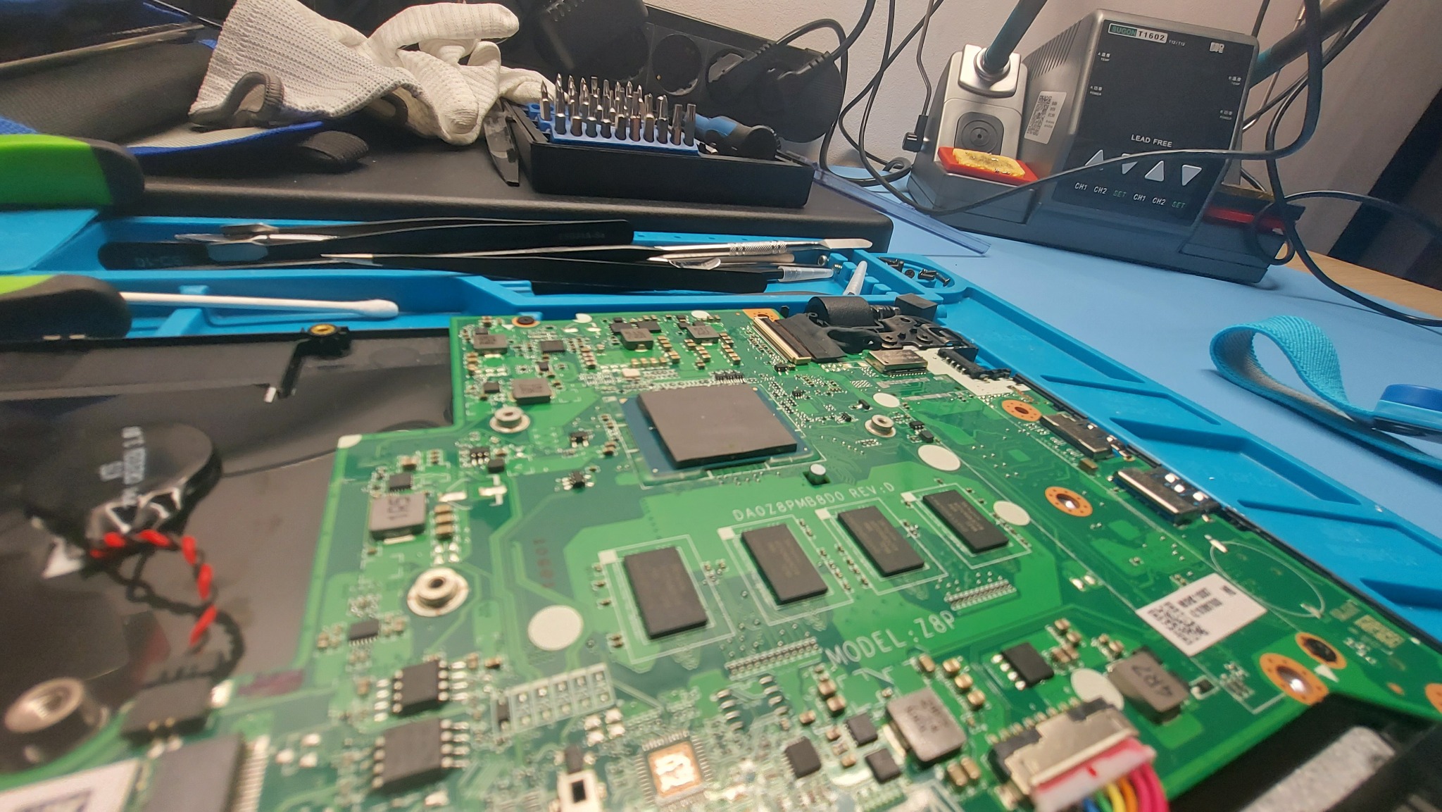 Płyta główna laptopa na niebieskiej macie serwisowej, widoczne narzędzia, pensety, śrubokręty, stacja lutownicza Sugon T1602, elementy elektroniczne i układy scalone, model Z8P, rewizja DAOZ8PMBBDO.