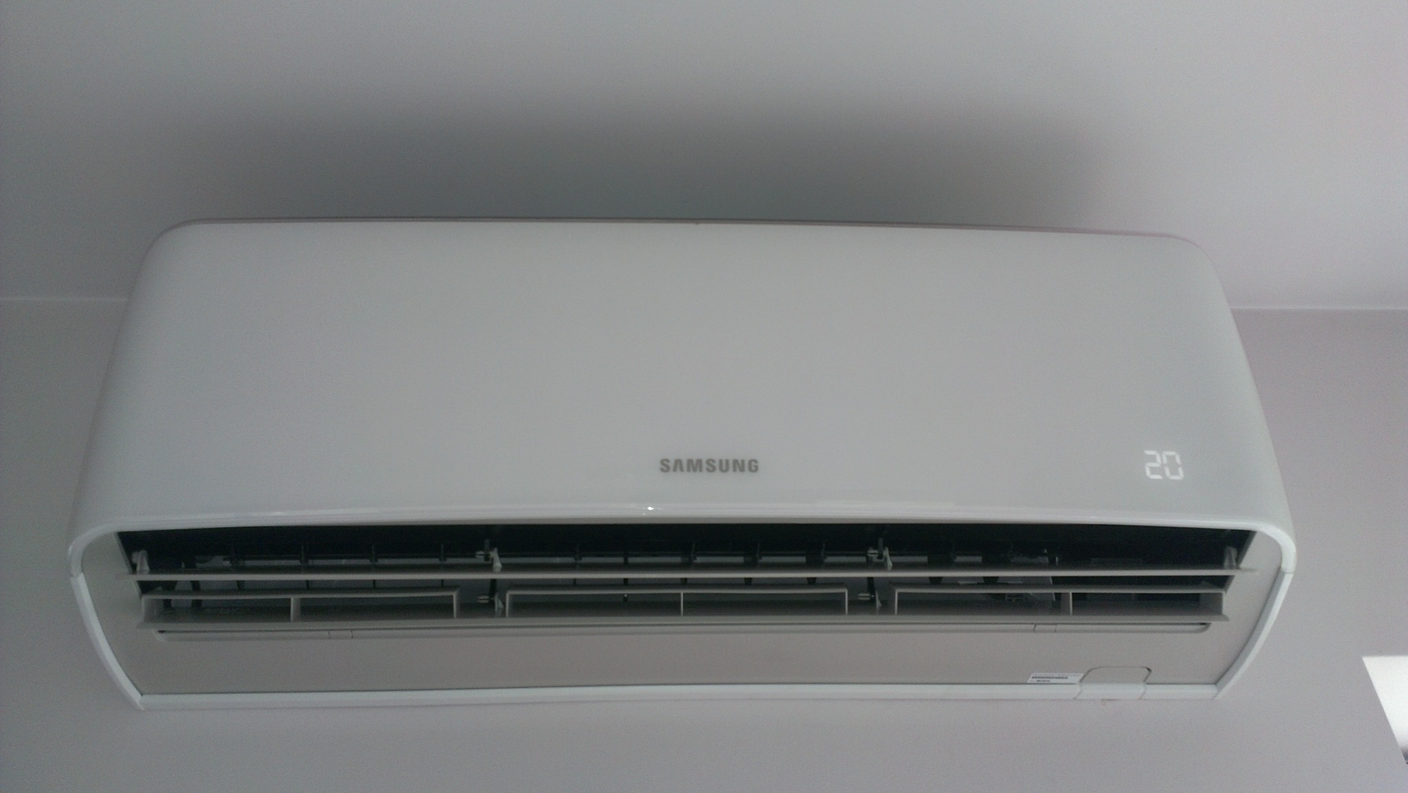 Biała klimatyzacja Samsung zamontowana na ścianie, wyświetlająca temperaturę 20 stopni Celsjusza.