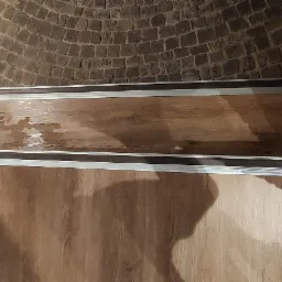 Wykończone wnętrze ze ścianami z cegły i drewnopodobną okładziną, widoczny fragment sufitu z cegły łukowej, okładzina zamontowana w ramie z metalowymi profilami.