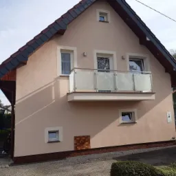 Elewacja domu z balkonem i balustradą szklaną ze stali nierdzewnej, widok z zewnątrz na jasną fasadę i balkon z mlecznym szkłem.