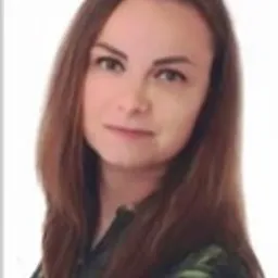 Portret kobiety z długimi brązowymi włosami, ubranej w bluzkę w kwiaty, na jasnym tle.