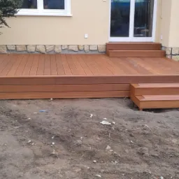 Nowoczesny taras kompozytowy z dwoma stopniami w Jaworze, prowadzący do drzwi balkonowych, z widocznym fragmentem elewacji wykończonej kamieniem.