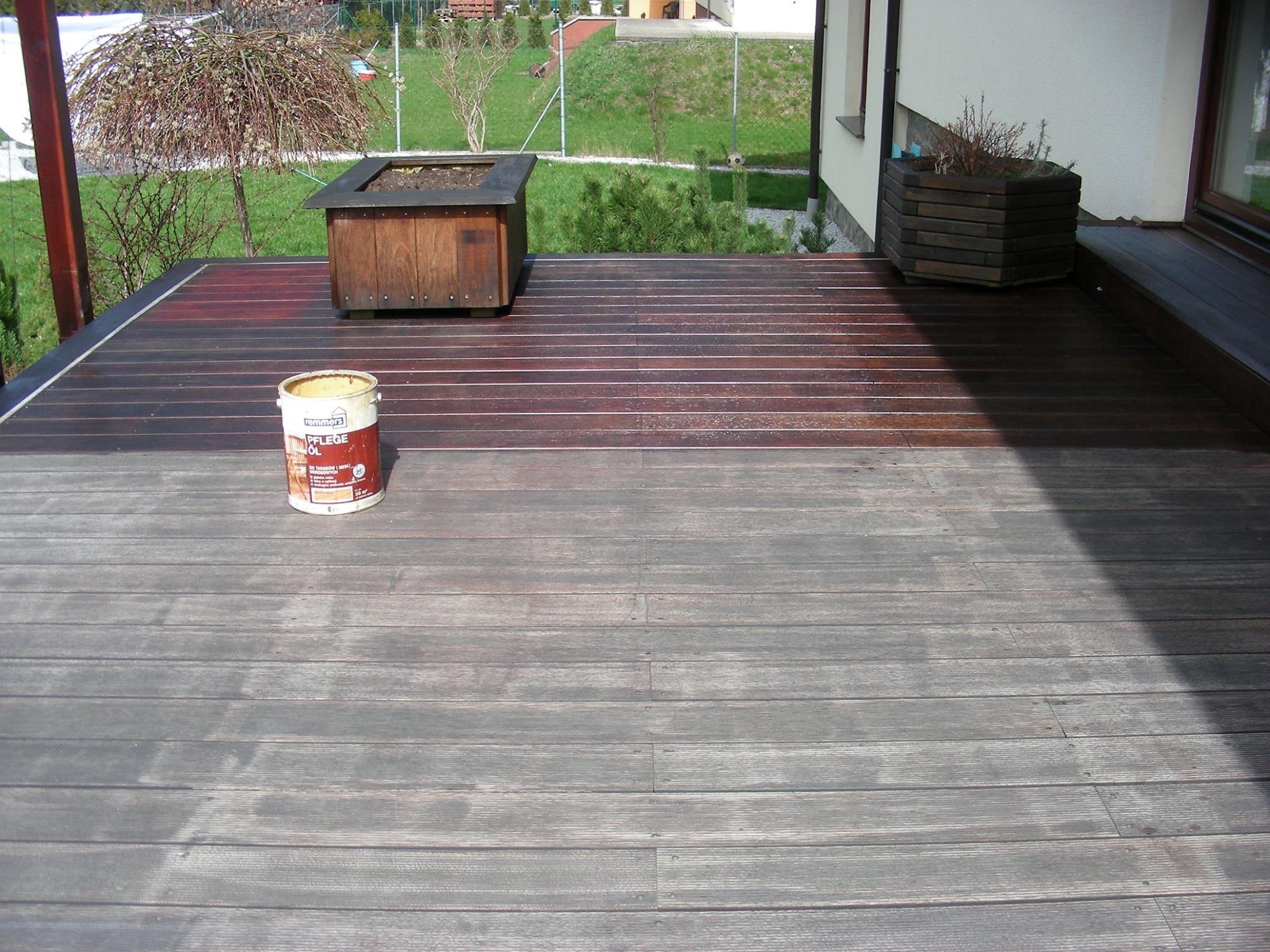 Częściowo odnowiony taras z desek, z widocznym wiadrem z olejem do drewna i donicami na rośliny.