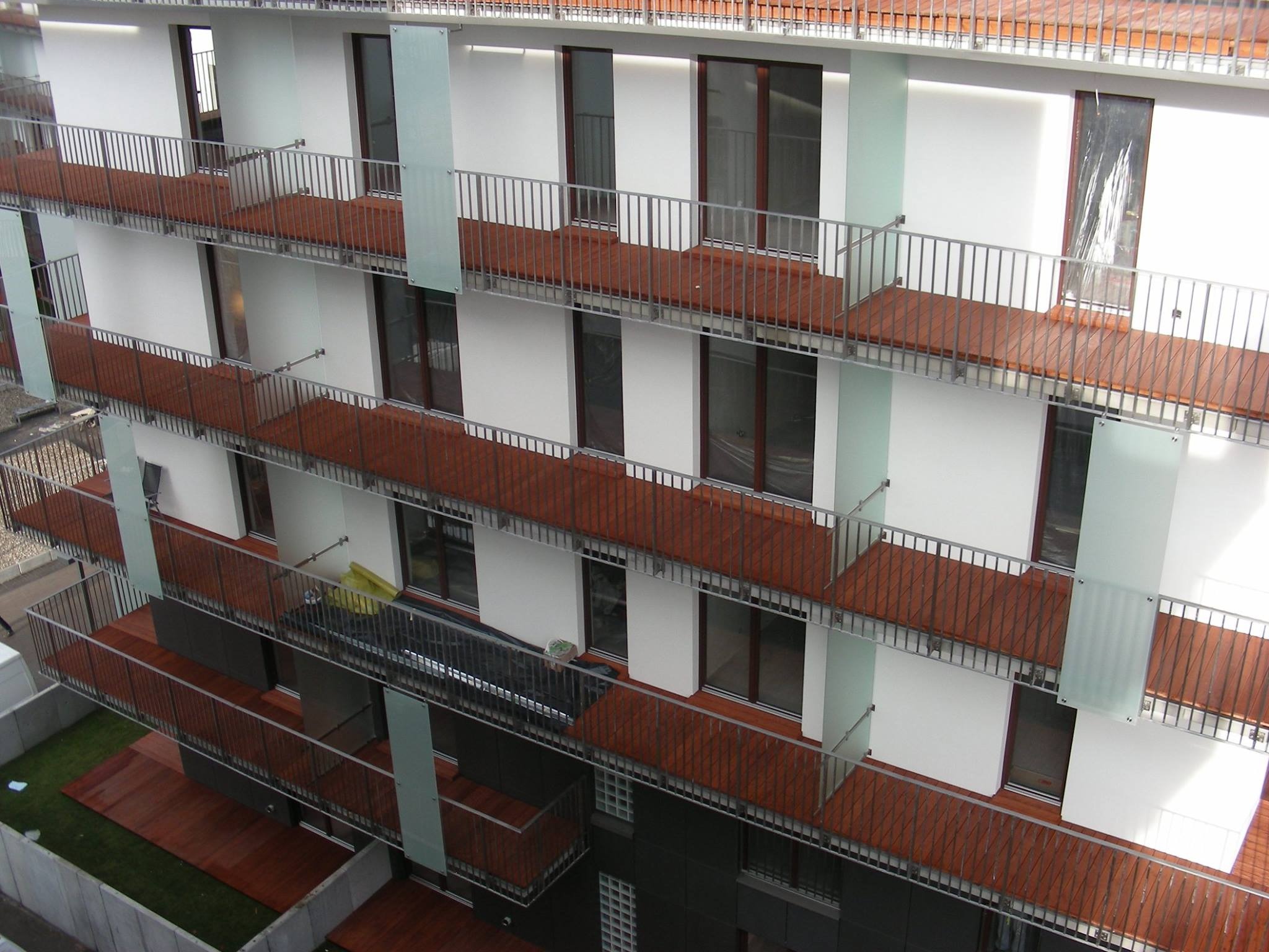 Wielopiętrowy budynek z balkonami wykończonymi drewnem, z metalowymi balustradami i szklanymi panelami, widok z góry.