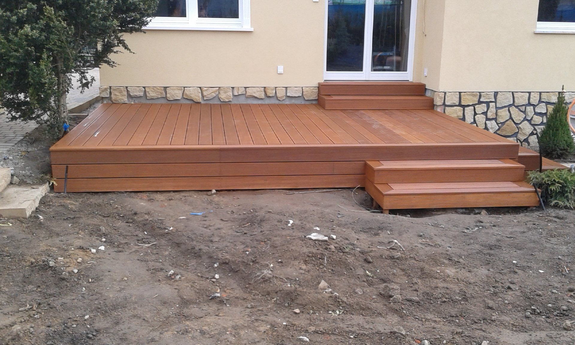 Nowoczesny taras kompozytowy z dwoma stopniami w Jaworze, prowadzący do drzwi balkonowych, z widocznym fragmentem elewacji wykończonej kamieniem.