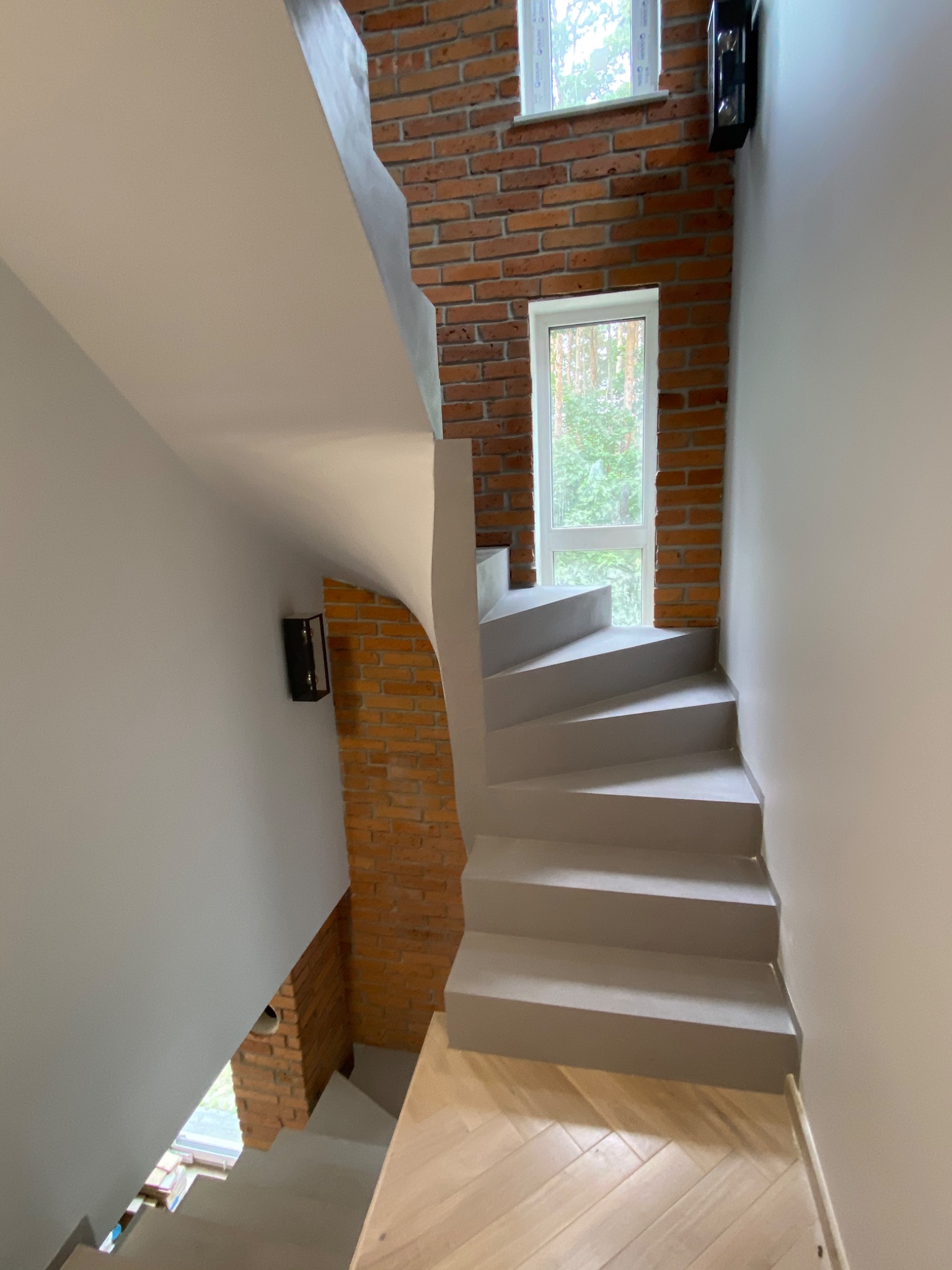 Nowoczesne schody w szarości z ceglaną ścianą, widok z góry, drewniana podłoga w jodełkę, minimalistyczne oświetlenie ścienne.