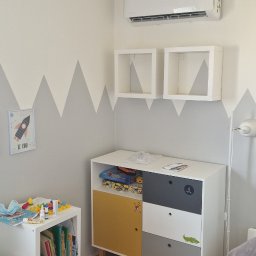 COOL PROJECT ŁUKASZ BIELAWSKI - Biały klimatyzator ścienny zamontowany w pokoju dziecięcym z dekoracją górską na ścianie, wiszącymi półkami i kolorową komodą.