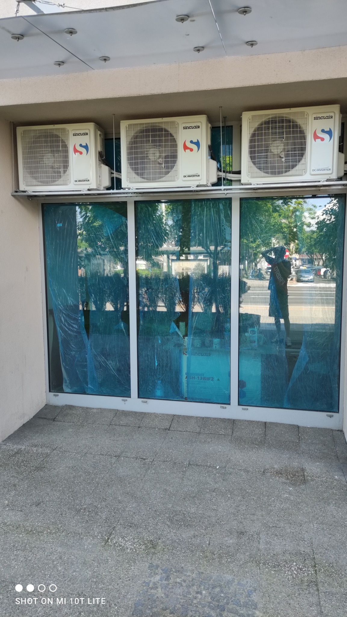 Trzy jednostki zewnętrzne klimatyzacji Sinclair zamontowane nad witryną sklepową, oklejone niebieską folią ochronną.