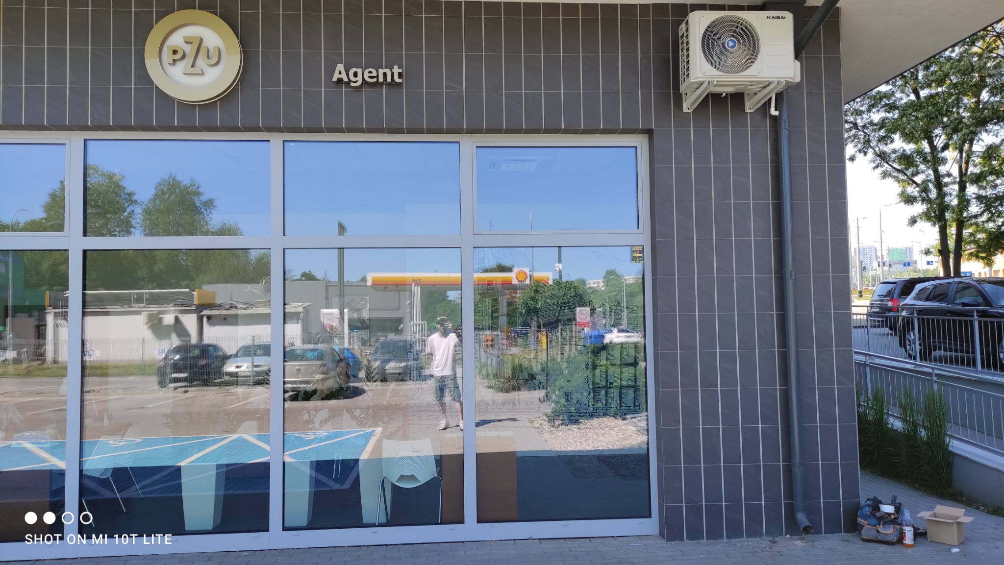 Biała jednostka zewnętrzna klimatyzacji Kaisa na szarej, kafelkowanej ścianie budynku biurowego z logo PZU Agent, widoczna instalacja odprowadzająca skropliny.