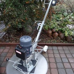 Dekor PUHB - Zacieraczka do betonu z silnikiem elektrycznym, ustawiona na kostce brukowej, z krzewem jarzębiny w tle.