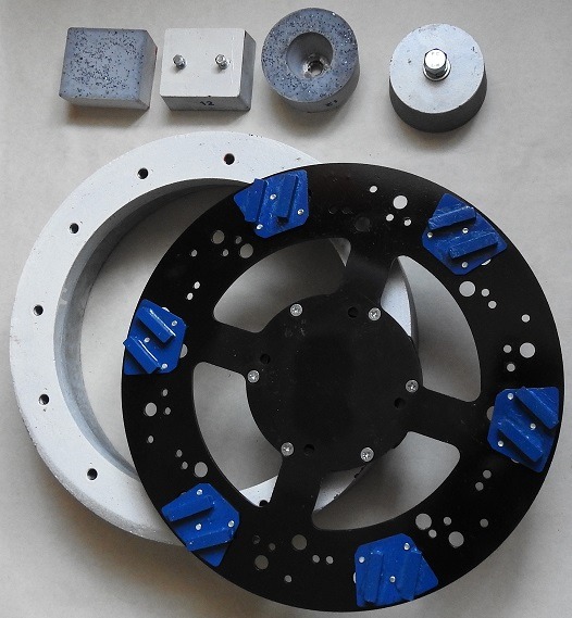 Zestaw narzędzi do szlifowania betonu: segmentowe ściernice z niebieskimi elementami ściernymi, betonowe bloczki i pierścień z otworami, ułożone na jasnym tle.