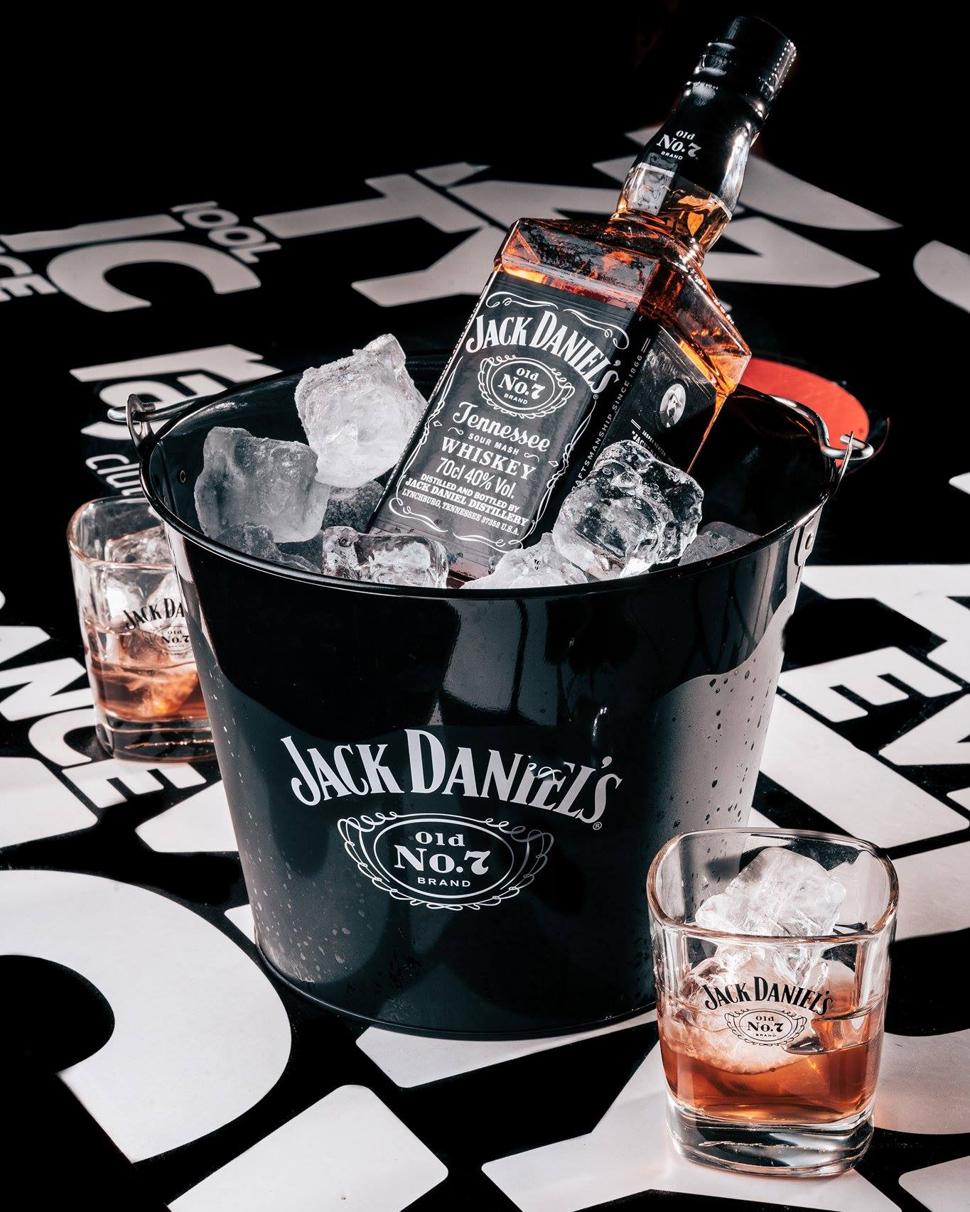 Butelka Jack Daniel's w wiaderku z lodem, dwa drinki z lodem na czarno-białym tle.