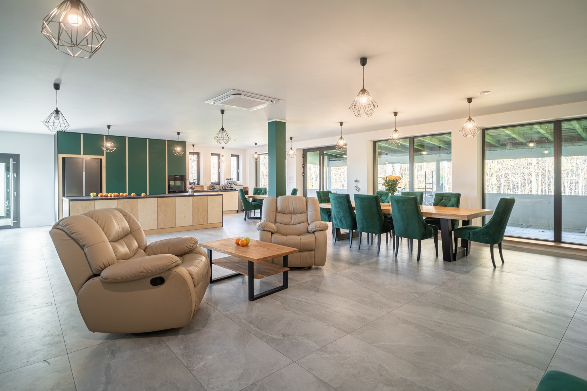 Przestronne wnętrze domu z otwartą kuchnią, jadalnią i strefą relaksu, w neutralnej kolorystyce z akcentami zieleni i drewnianymi elementami wykończenia.