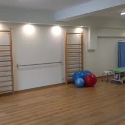 Sala do ćwiczeń z drabinkami gimnastycznymi, piłkami rehabilitacyjnymi, leżanką i parawanem.