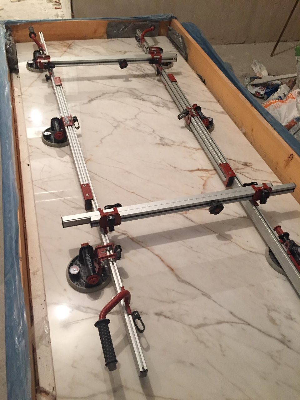 Marmurowa płyta zabezpieczona ramą z przyssawkami i aluminiowymi profilami do precyzyjnego cięcia, widoczne narzędzia glazurnicze.