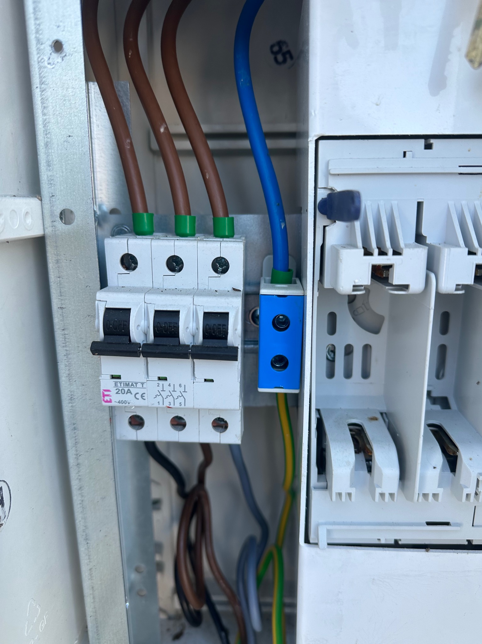 Rozdzielnica elektryczna z zainstalowanymi bezpiecznikami i przewodami w kolorach: brązowym, niebieskim i żółto-zielonym. Widoczne śruby mocujące i oznaczenia na bezpiecznikach.