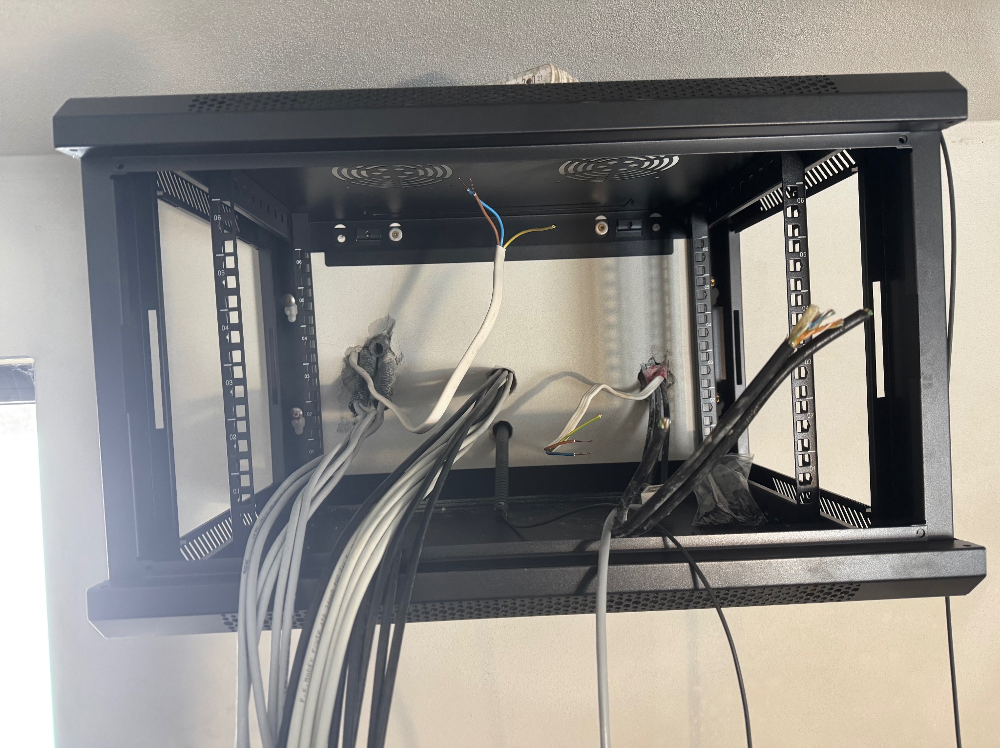 Szafa RACK w trakcie montażu: widoczne kable wchodzące do szafy, otwory w ścianie i elementy mocujące. Ujęcie z bliska, skupione na wnętrzu szafy i przewodach.