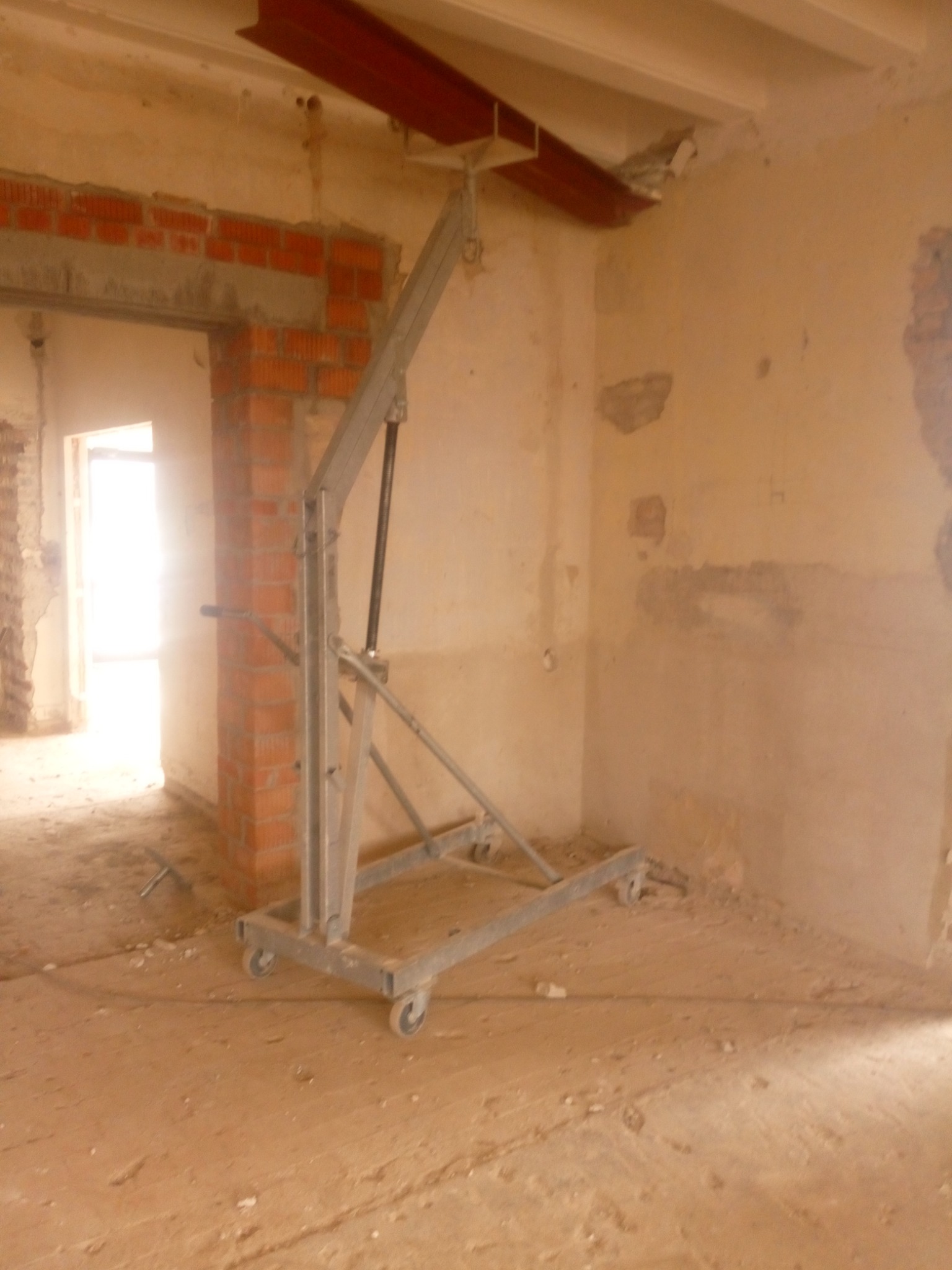 Wnętrze w trakcie remontu z podnośnikiem do montażu stalowej belki pod stropem, widoczne fragmenty muru z cegły i surowy stan ścian.
