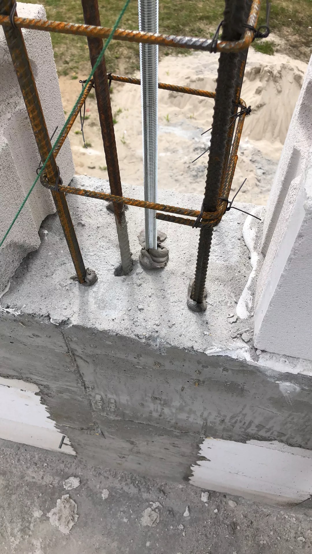 Fragment ściany z betonu komórkowego z widocznym zbrojeniem pionowym i poziomym, oraz gwintowanym prętem stalowym. Zbrojenie związane drutem. Widoczne niedociągnięcia w wypełnieniu spoin między...