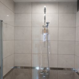 Stanisław Remonty i wykończenia - Wykończona łazienka z beżowymi płytkami, szklanym panelem prysznicowym i chromowaną armaturą, widoczne detale wykończenia.