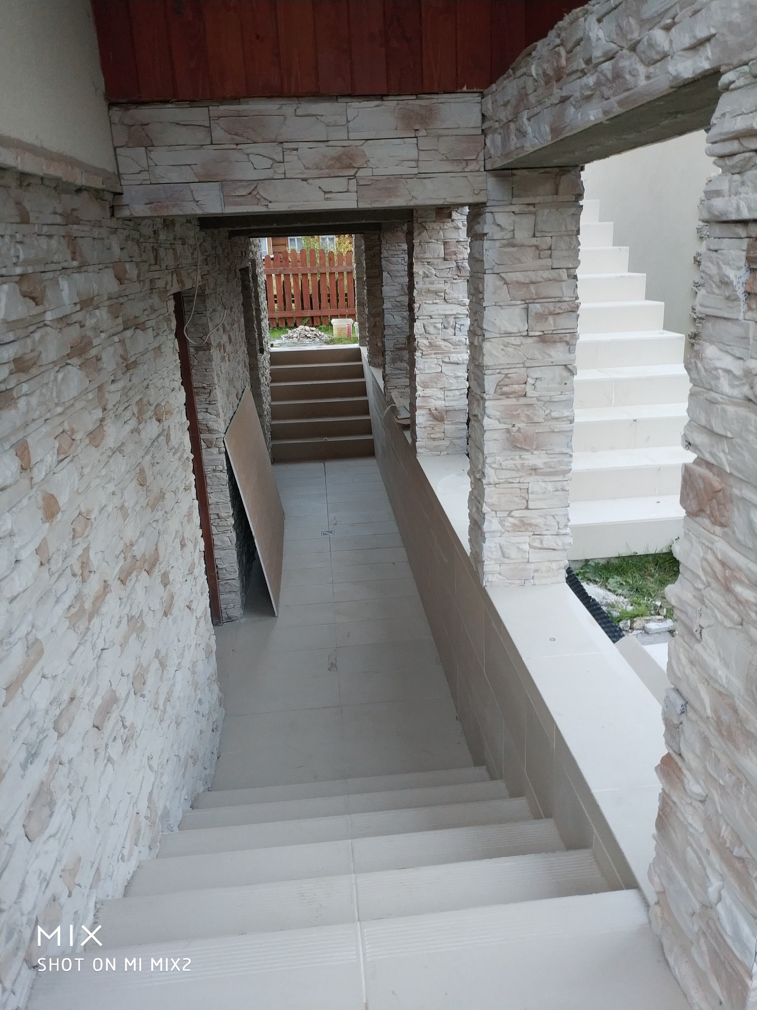 Wykończone schody zewnętrzne z jasnymi płytkami ceramicznymi i okładziną z kamienia dekoracyjnego na ścianach i filarach, widok z góry na dół.