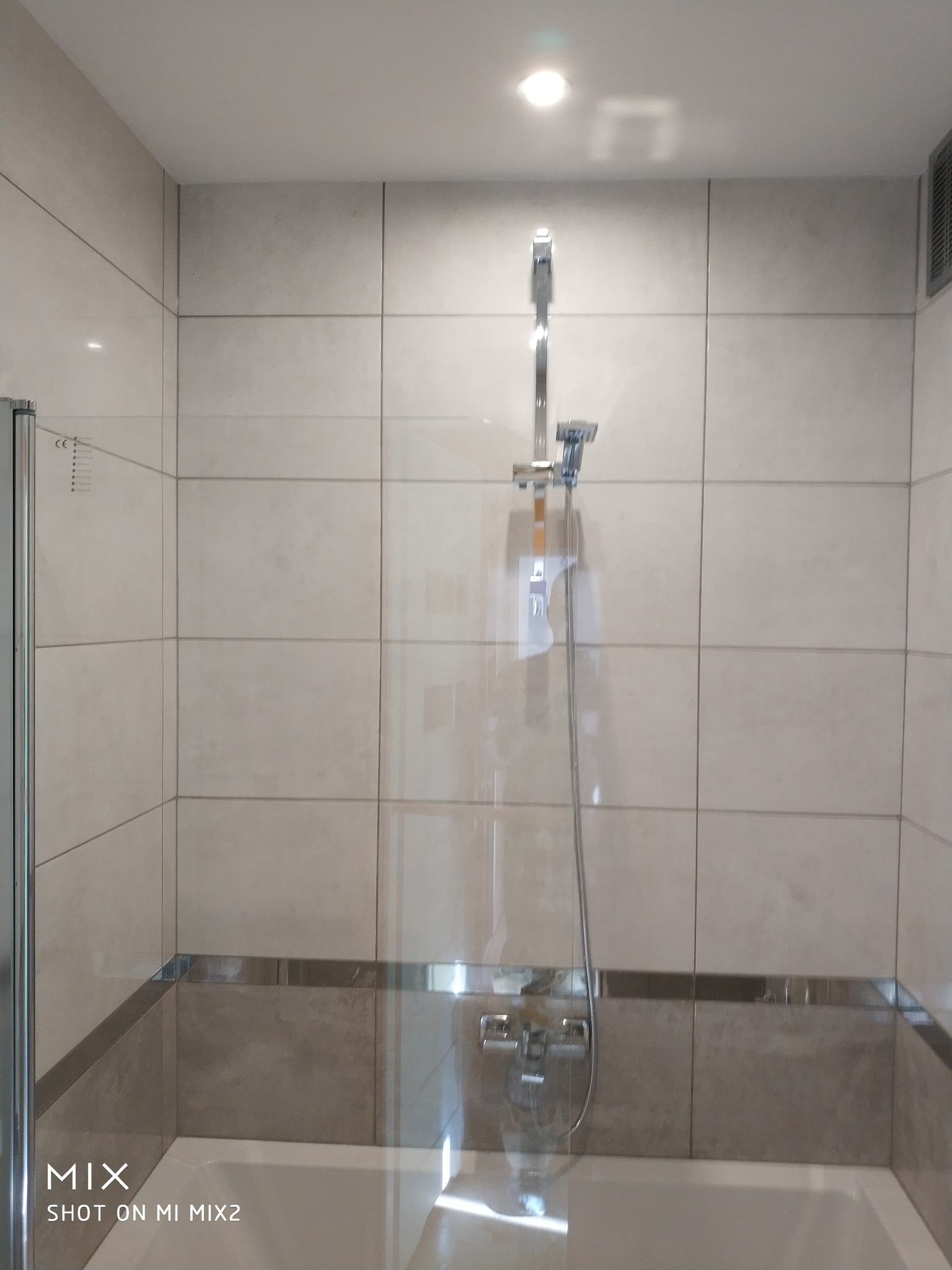 Wykończona łazienka z beżowymi płytkami, szklanym panelem prysznicowym i chromowaną armaturą, widoczne detale wykończenia.