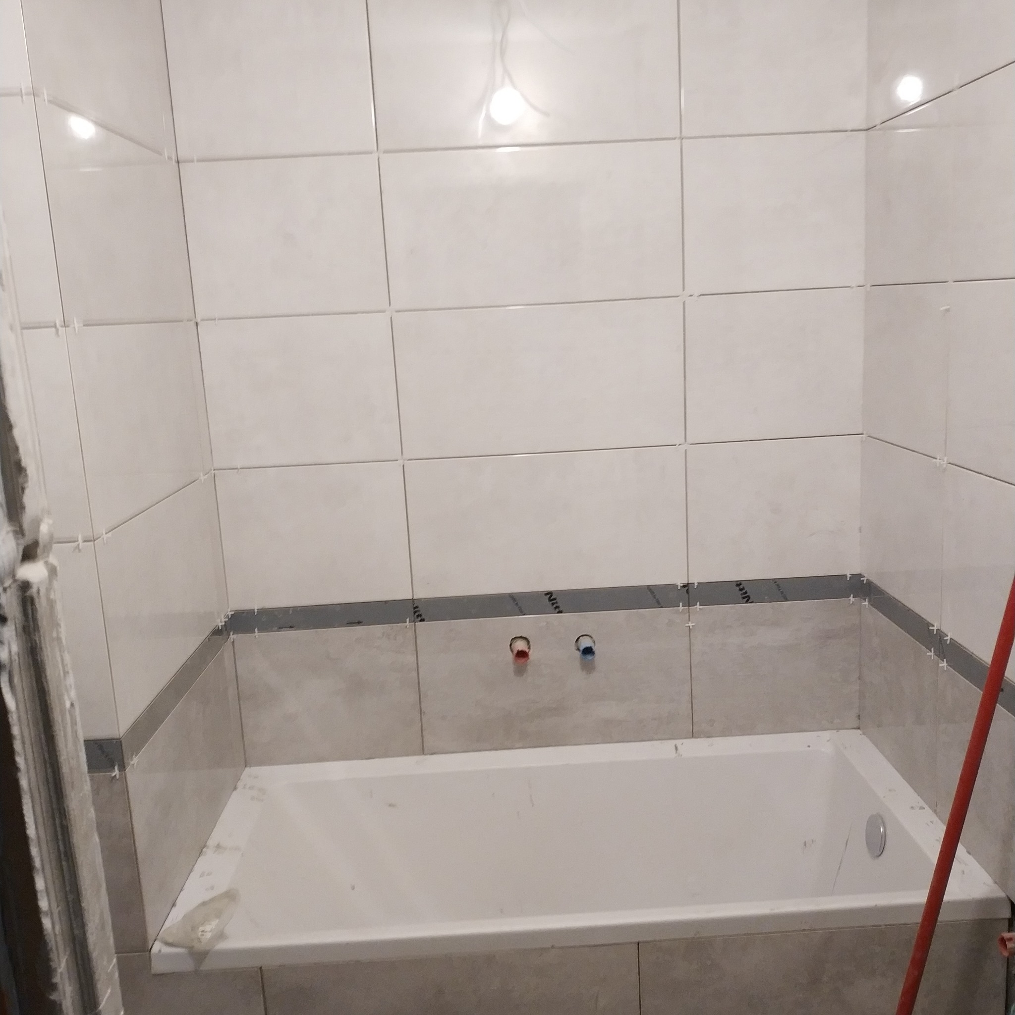 Wanna obudowana płytkami w trakcie prac w Łopusznej, widoczne krzyżyki dystansowe i fragment rury.