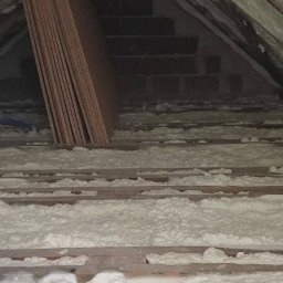 FIRMA HANDLOWO-USŁUGOWA Bartłomiej Biernat - Poddasze w Żłobku w trakcie ocieplania: biała pianka izolacyjna wypełnia przestrzeń między krokwiami, widoczne deski stropowe, rura wentylacyjna i płyty kartonowo-gipsowe przygotowane do montażu.