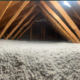 FIRMA HANDLOWO-USŁUGOWA Bartłomiej Biernat - Poddasze z drewnianą konstrukcją krokwiową wypełnione warstwą izolacyjną z wełny mineralnej, widoczna skala pomiarowa grubości izolacji.