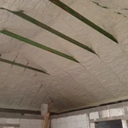 Poddasze pokryte warstwą izolacyjną z pianki, widoczne drewniane belki stropowe, surowy stan wykończenia ścian z bloczków.